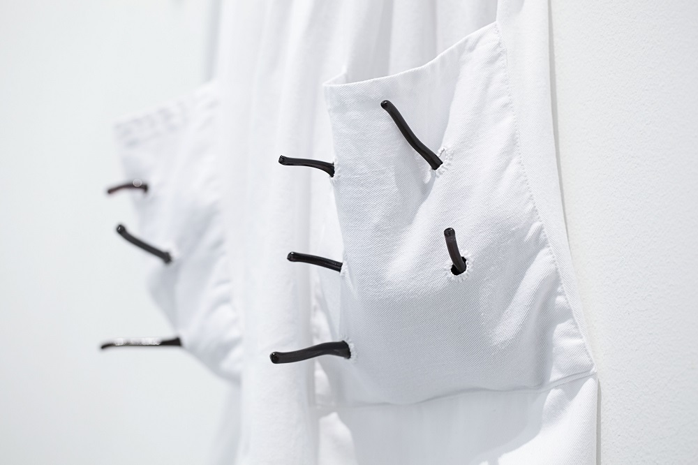 Hand-blown glass yams poking through white apron pockets made by artist Yhonnie Scarce